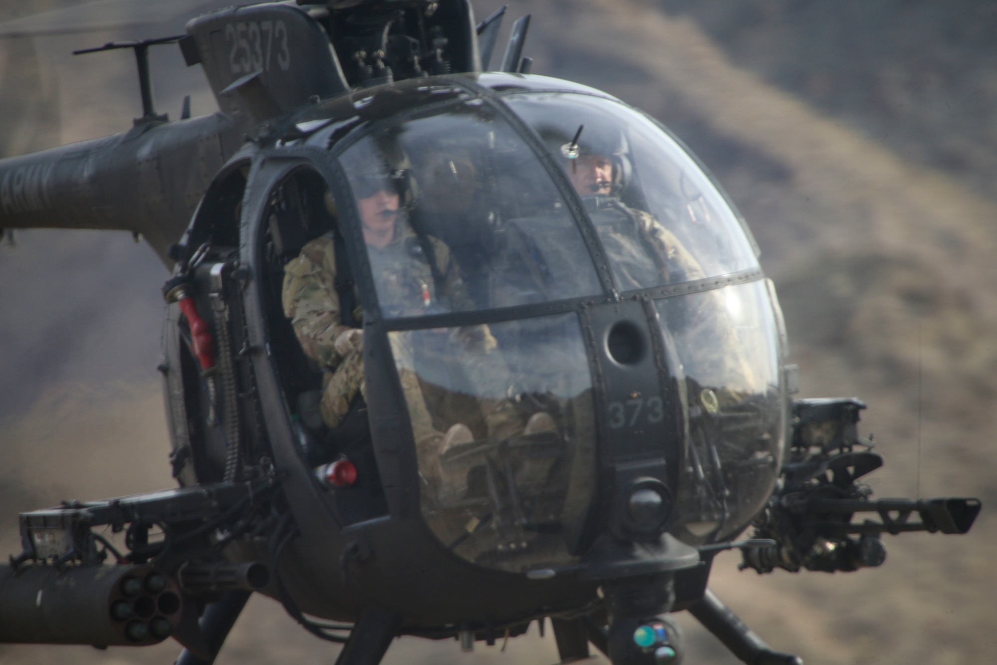 Close view of AH-6 Little Bird number 373 in flight with crew visible through the bubble canopy.