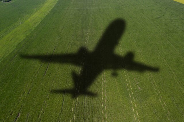 Shadow of a twin-engine aircraft crossing a green field below.