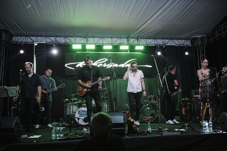 Live musical performance by a band at a festival in the evening under bright stage lights