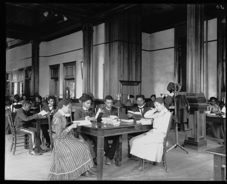 Interior view of library reading room with male and female students sitting at tables reading at the Tuskegee Institute