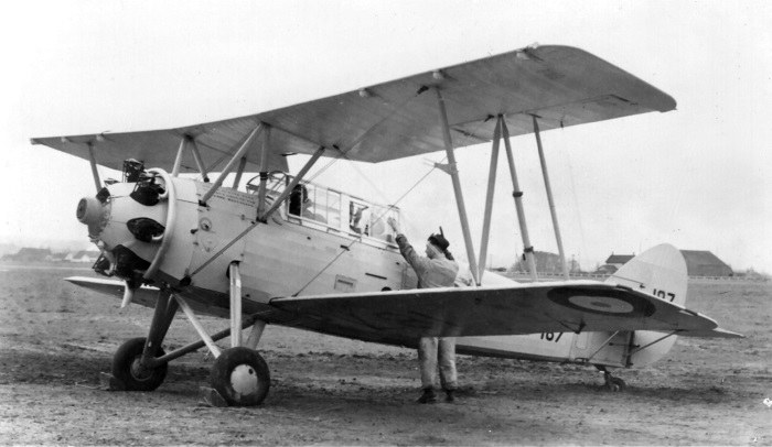 Black-and-white Avro 621 Tutor 107 on the ground with a crewman beside the cockpit.