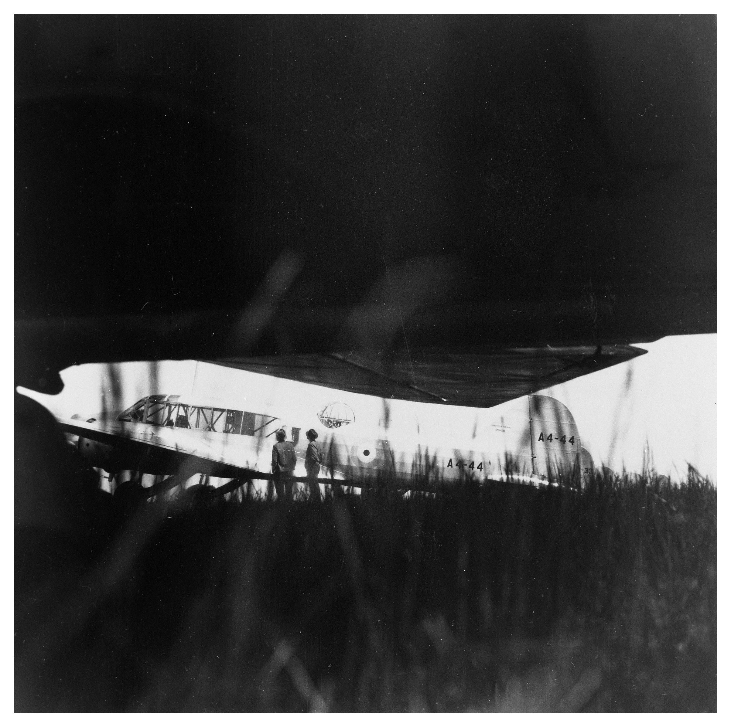 Dark black-and-white image of Avro Anson A4-44 partly hidden beneath a large wing shadow.
