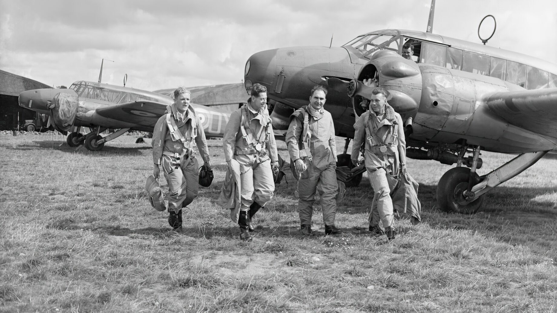 Black-and-white photo of aircrew walking in front of parked Avro Ansons.