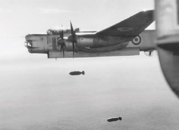 Black-and-white view of an Avro Lincoln in flight with two bombs falling below.
