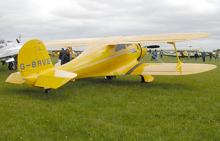 Beechcraft Staggerwing in yellow livery on grass, showing the distinctive staggered-wing biplane design associated with early Beechcraft production.