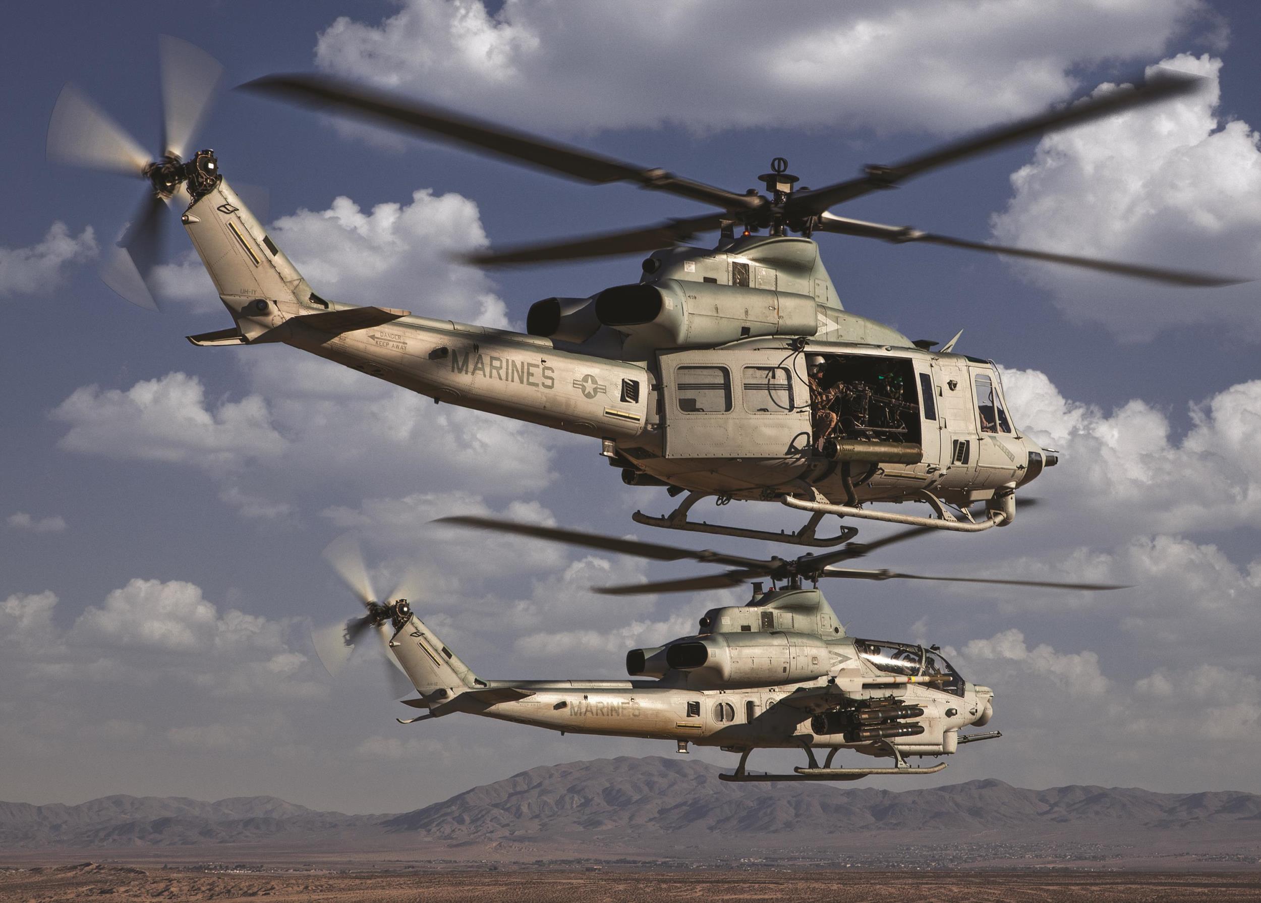 Bell UH-1Y and AH-1Z Marine helicopters flying in formation above desert terrain.