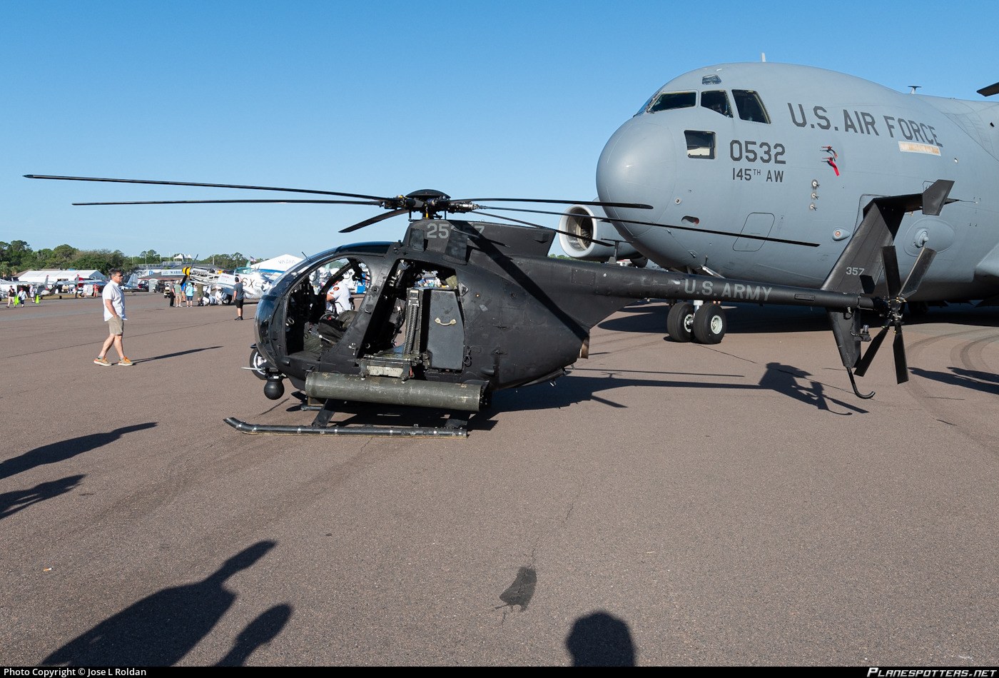Dark AH-6 Little Bird parked on a ramp beside a U.S. Air Force tanker aircraft.