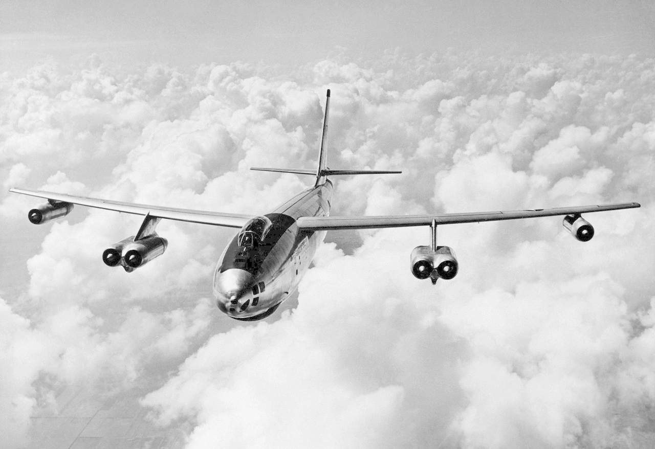 Black-and-white front view of a Boeing B-47 flying above clouds.