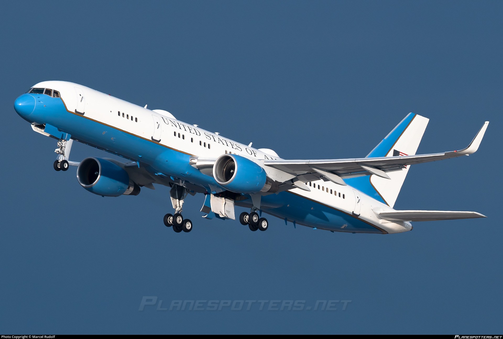 Blue-and-white Boeing C-32 flying with landing gear extended.