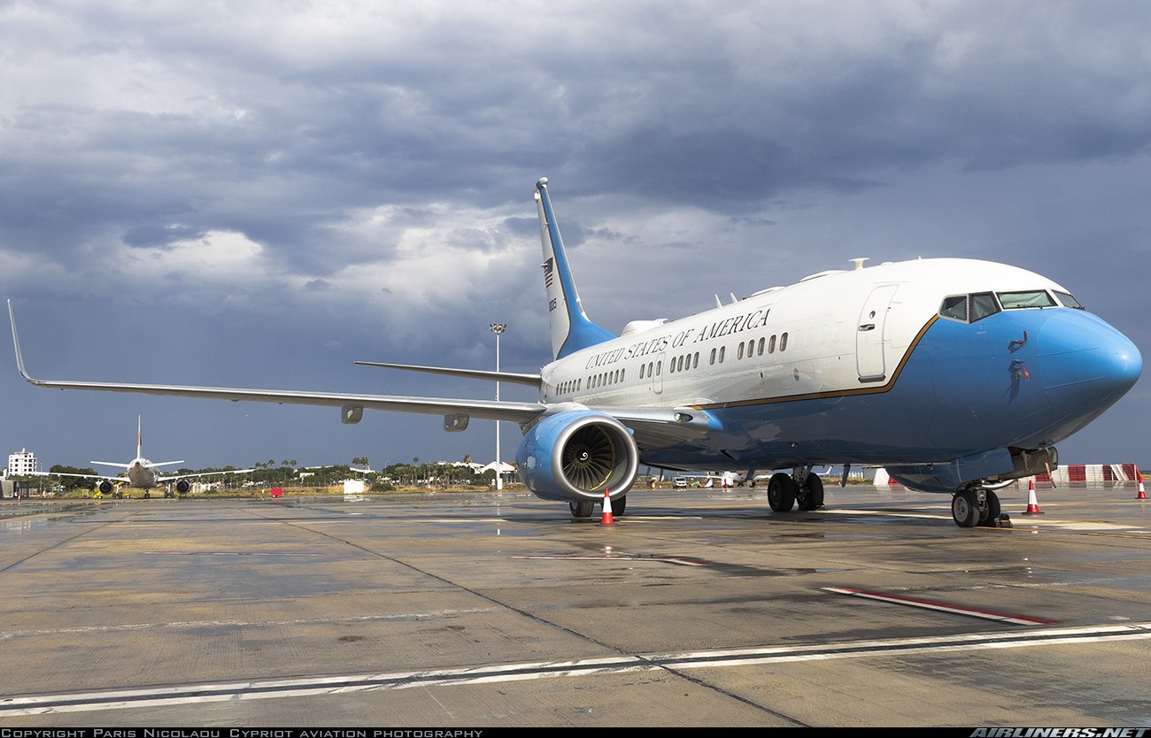 Blue-and-white Boeing C-40 parked on a wet ramp under storm clouds.