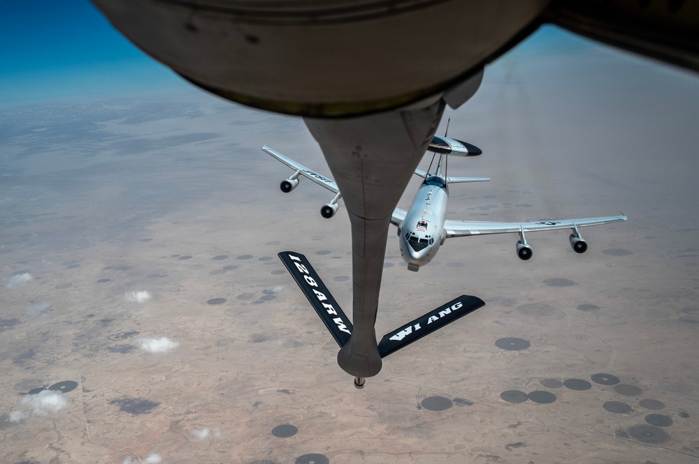Boeing E-3 Sentry flying below a tanker boom over desert terrain.