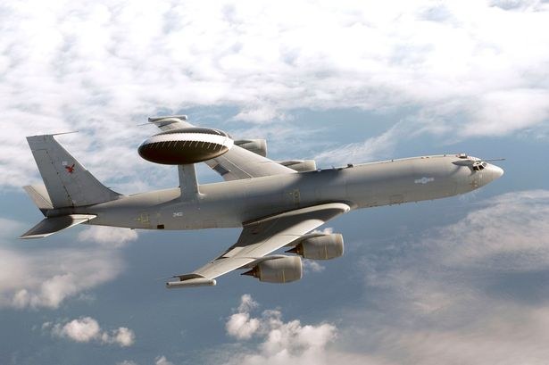 Gray Boeing E-3 Sentry flying above clouds with radar dome and four engines visible.
