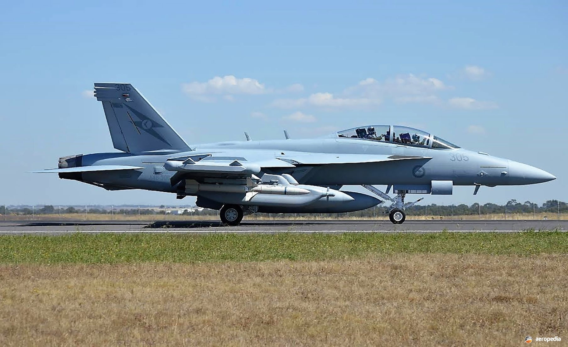 Gray Boeing EA-18G Growler 303 rolling on runway in side view.