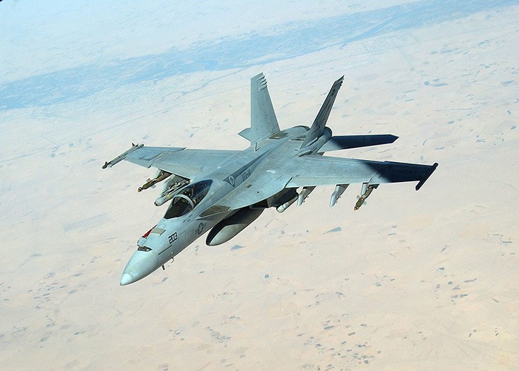 Gray Boeing F/A-18 Super Hornet 213 flying above desert terrain.