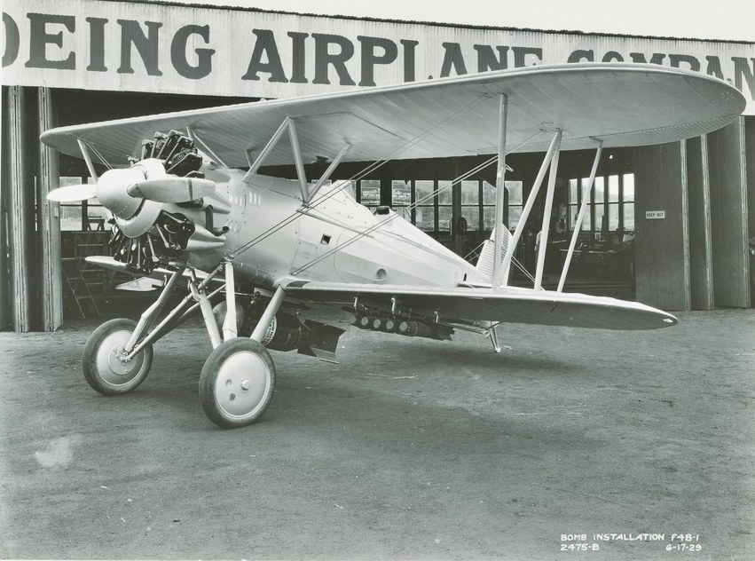 Boeing F4B-1 biplane outside a Boeing building with small bombs mounted underneath.