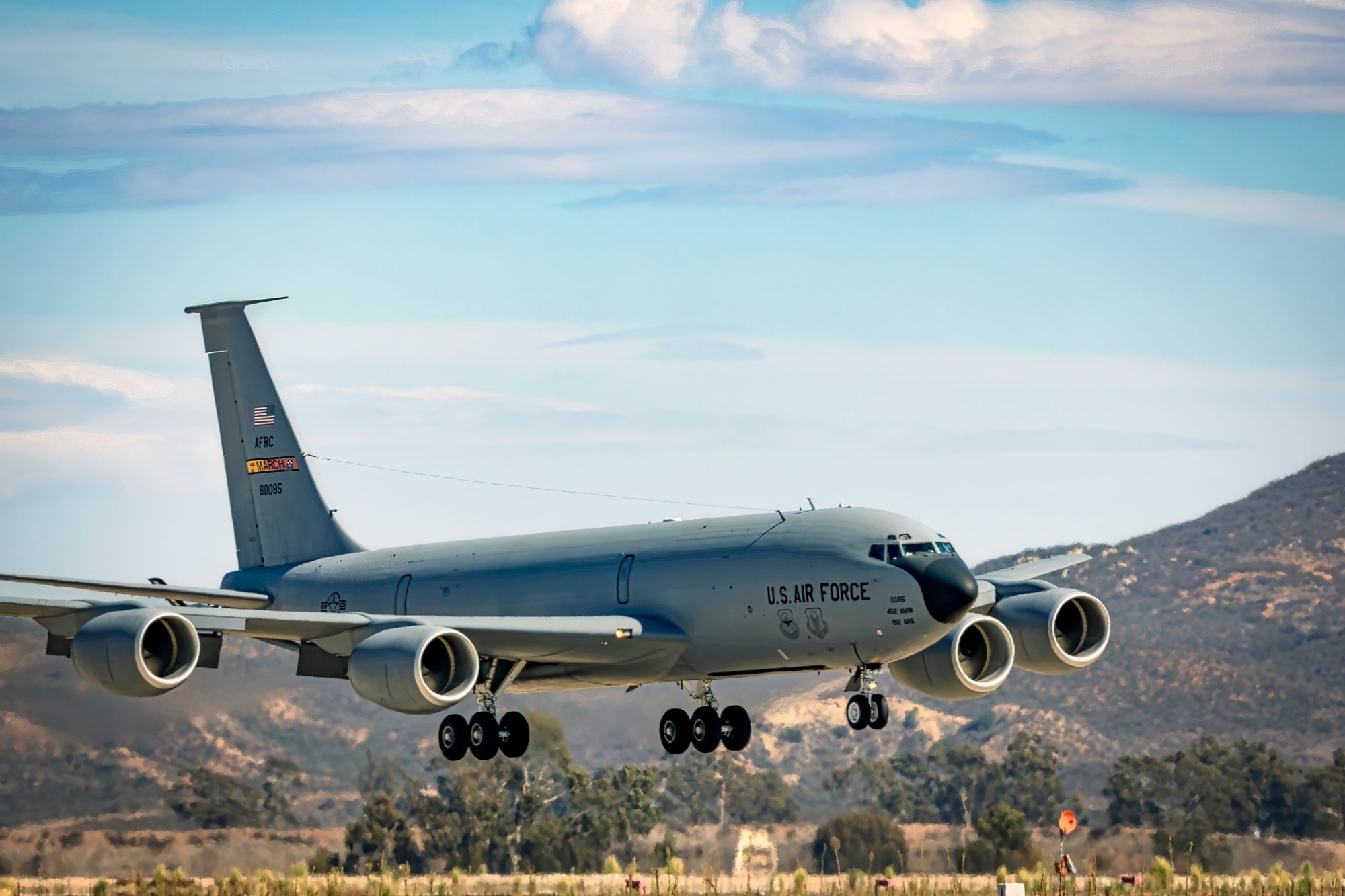 KC-135 Stratotanker approaching with landing gear extended over hills.