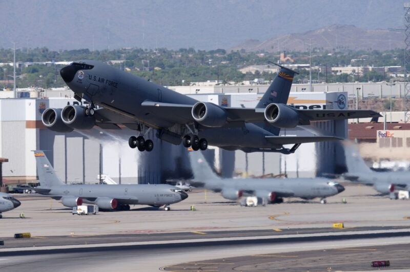 KC-135 Stratotanker climbing away from a runway with airport buildings below.