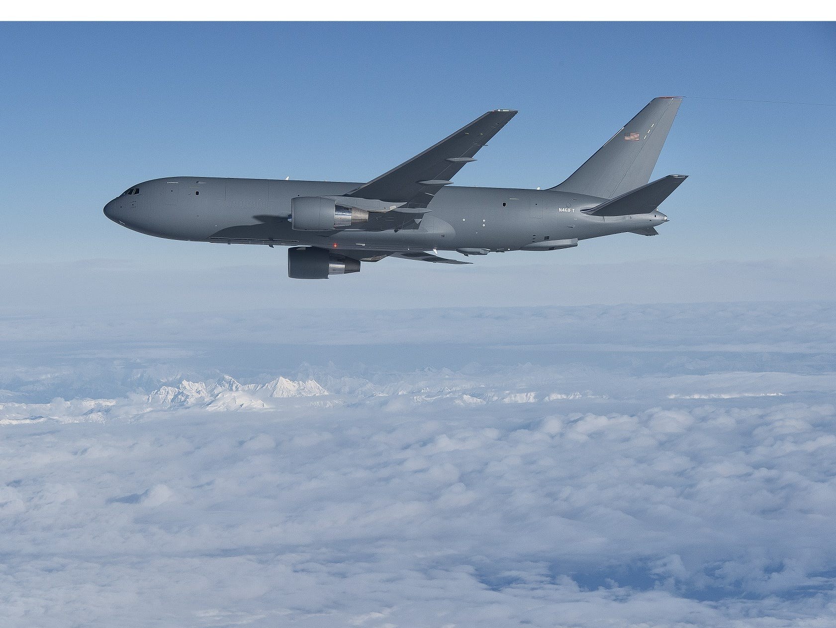 KC-46 Pegasus flying in profile above clouds and snowy mountains.