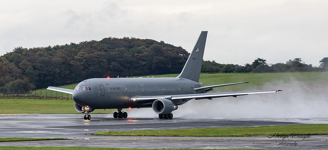 KC-46 Pegasus rolling on a wet runway with spray behind the landing gear.