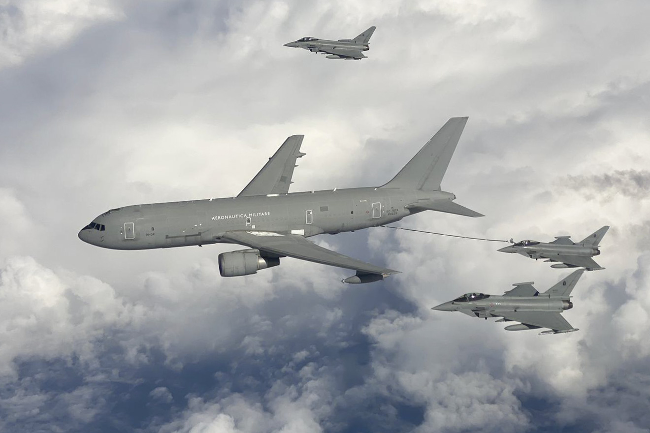 Italian KC-767A flying among three fighters in cloudy sky.
