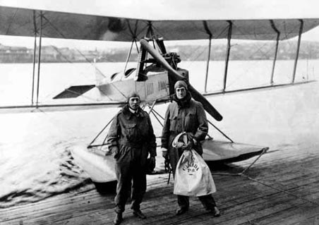 Two people standing on a dock in front of a Boeing Model C floatplane.