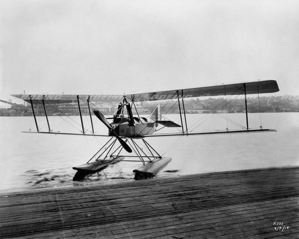 Boeing Model C floatplane moving on water beside a wooden dock.