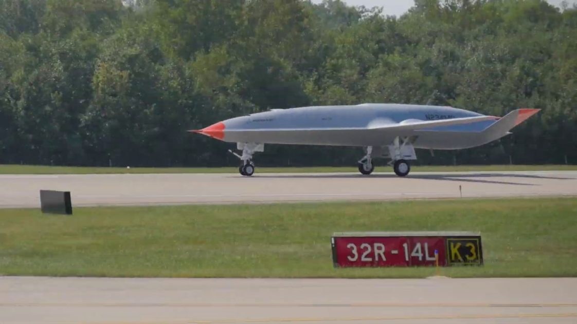 Boeing MQ-25 Stingray test aircraft taxiing on a runway with orange nose and tail markings.