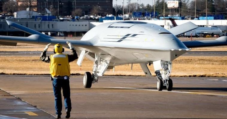 Boeing MQ-25 Stingray taxiing toward a ground crew member on a paved ramp.