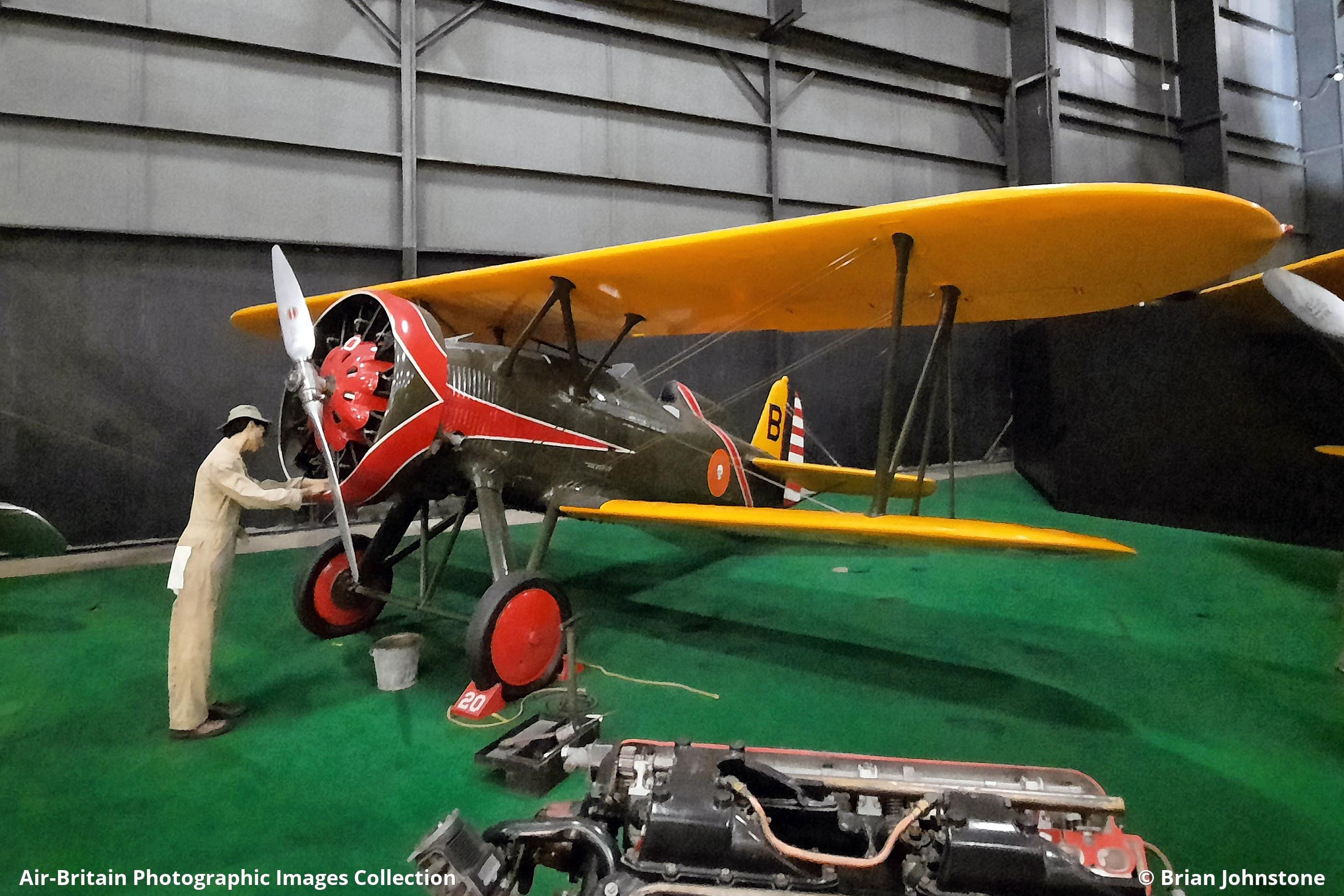 Boeing P-12 biplane displayed indoors with a mechanic figure by the propeller.