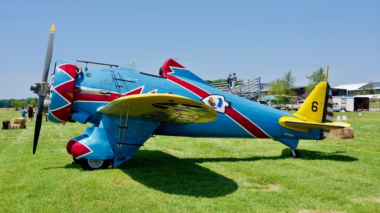 Blue and yellow Boeing P-26 Peashooter marked 6 parked on grass.