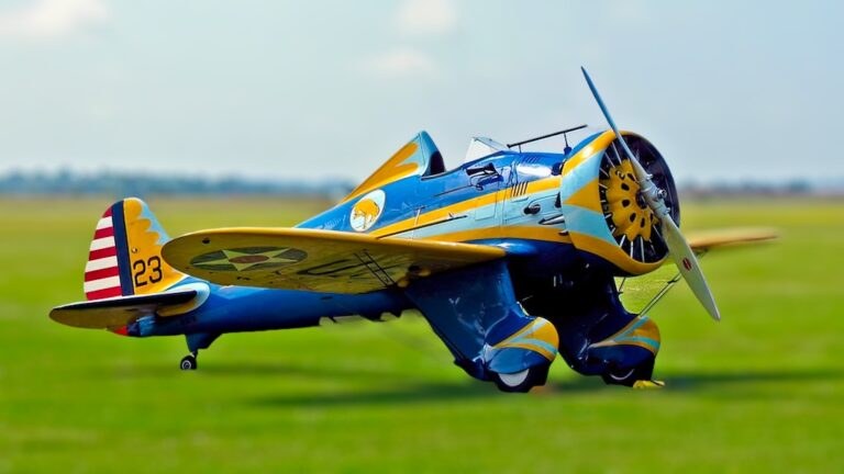 Blue and yellow Boeing P-26 Peashooter marked 23 on grass.