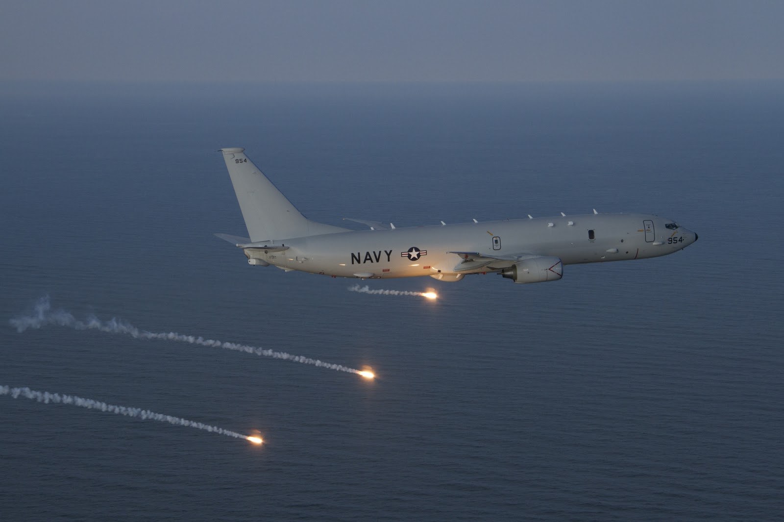 U.S. Navy P-8 Poseidon 954 releasing bright flares over water.