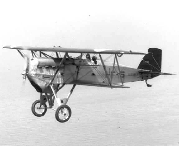Black-and-white side view of a Boeing PW-9 biplane flying with landing gear fixed down.