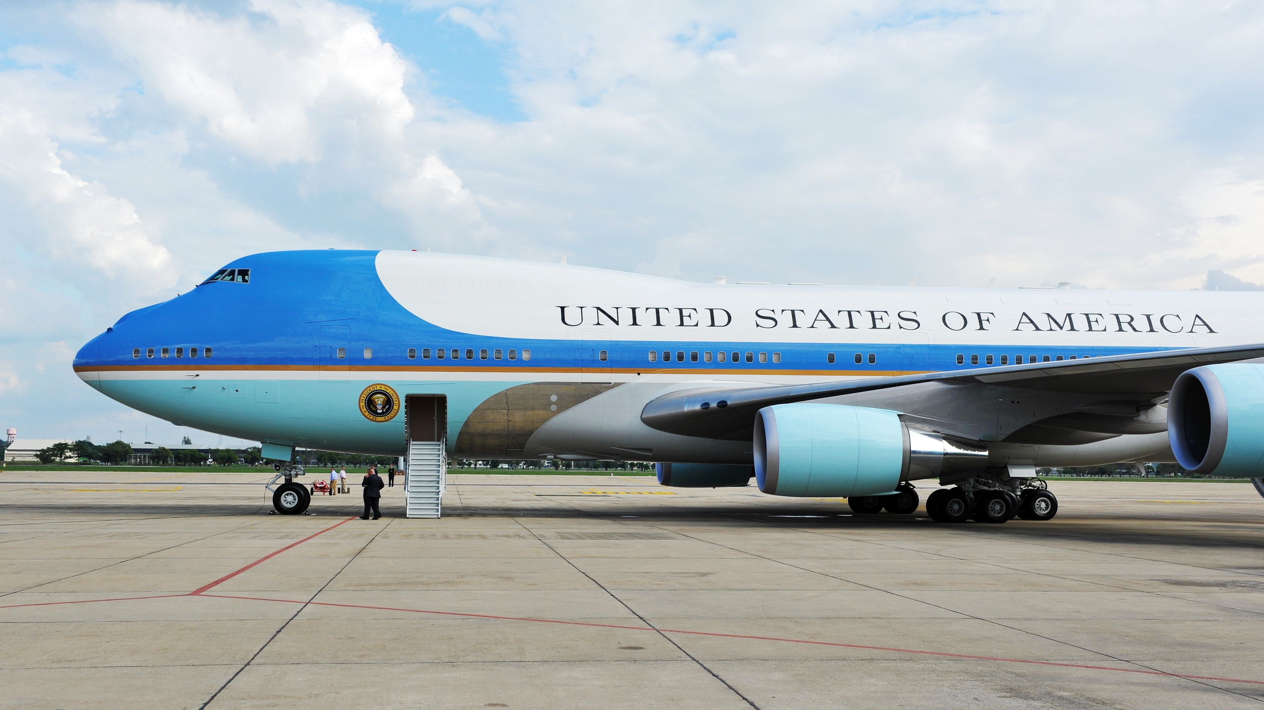 Close cropped side view of a blue-and-white VC-25 fuselage below bright clouds.