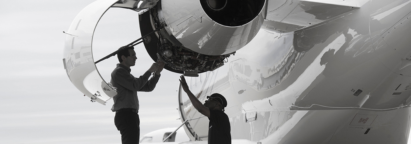 Two technicians working on an opened rear-mounted jet engine on a Bombardier aircraft.