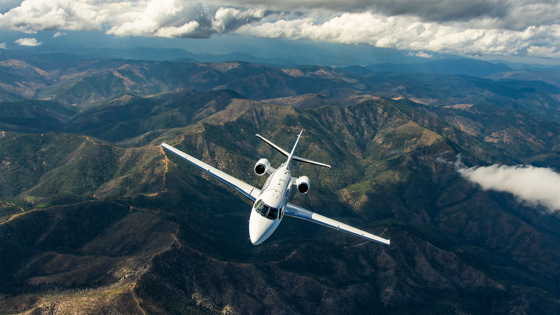 White Cessna Citation Ascend business jet banking over mountains