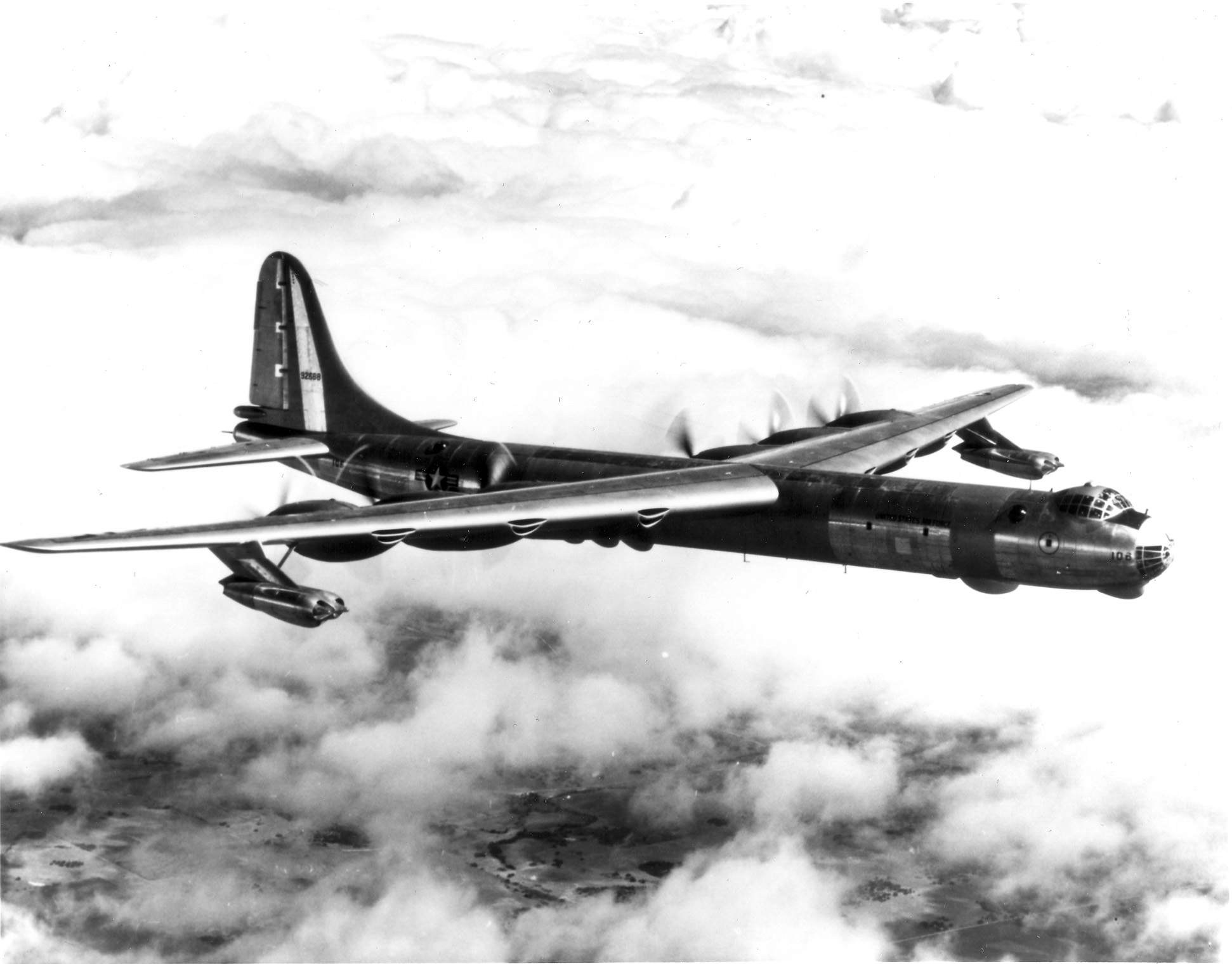 Black-and-white side view of Convair B-36 Peacemaker number 108 flying above clouds.