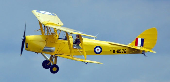 Yellow de Havilland DH.82 Tiger Moth K-2572 flying against a blue sky.