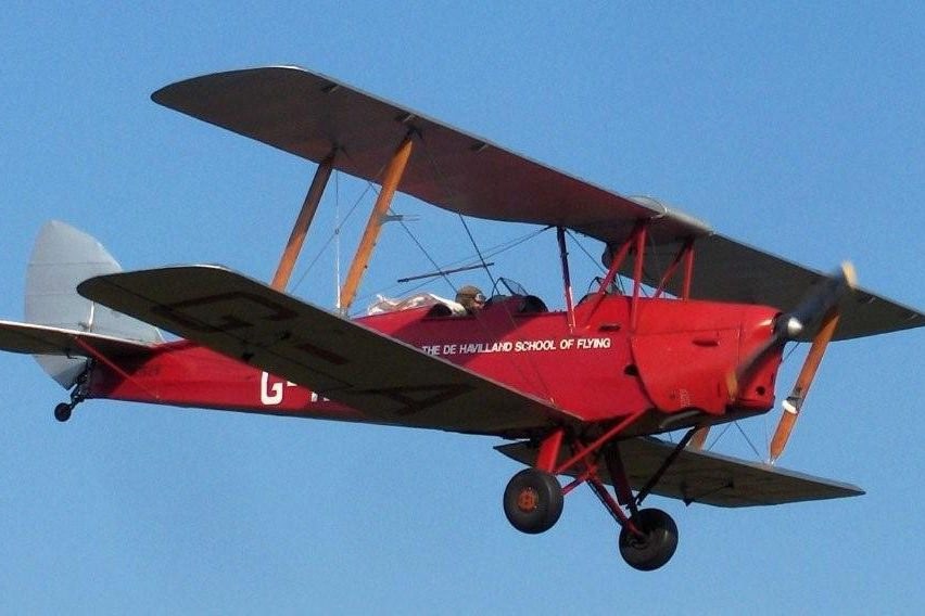 Red de Havilland school Tiger Moth flying against a blue sky.