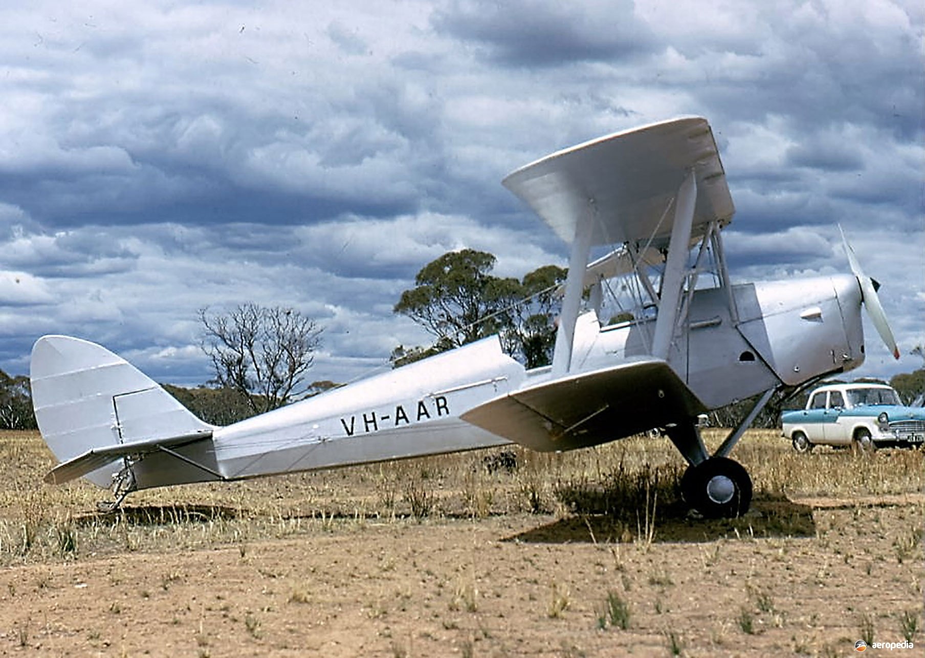 White de Havilland Tiger Moth VH-AAR parked in a dry field.