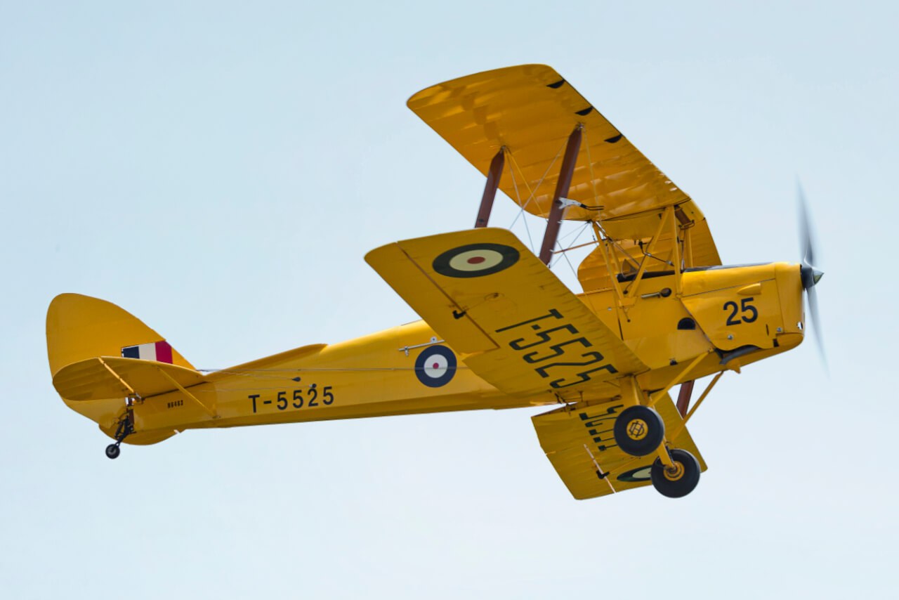 Yellow de Havilland Tiger Moth T-5525 flying overhead with roundels visible.