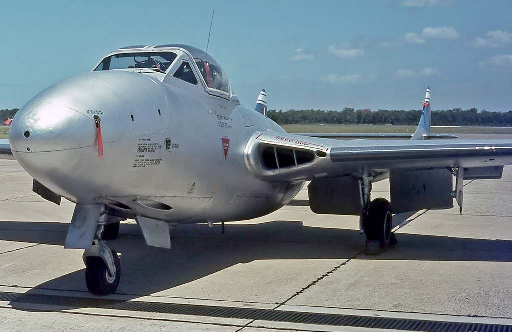 Close front view of a silver de Havilland Vampire on a concrete ramp.
