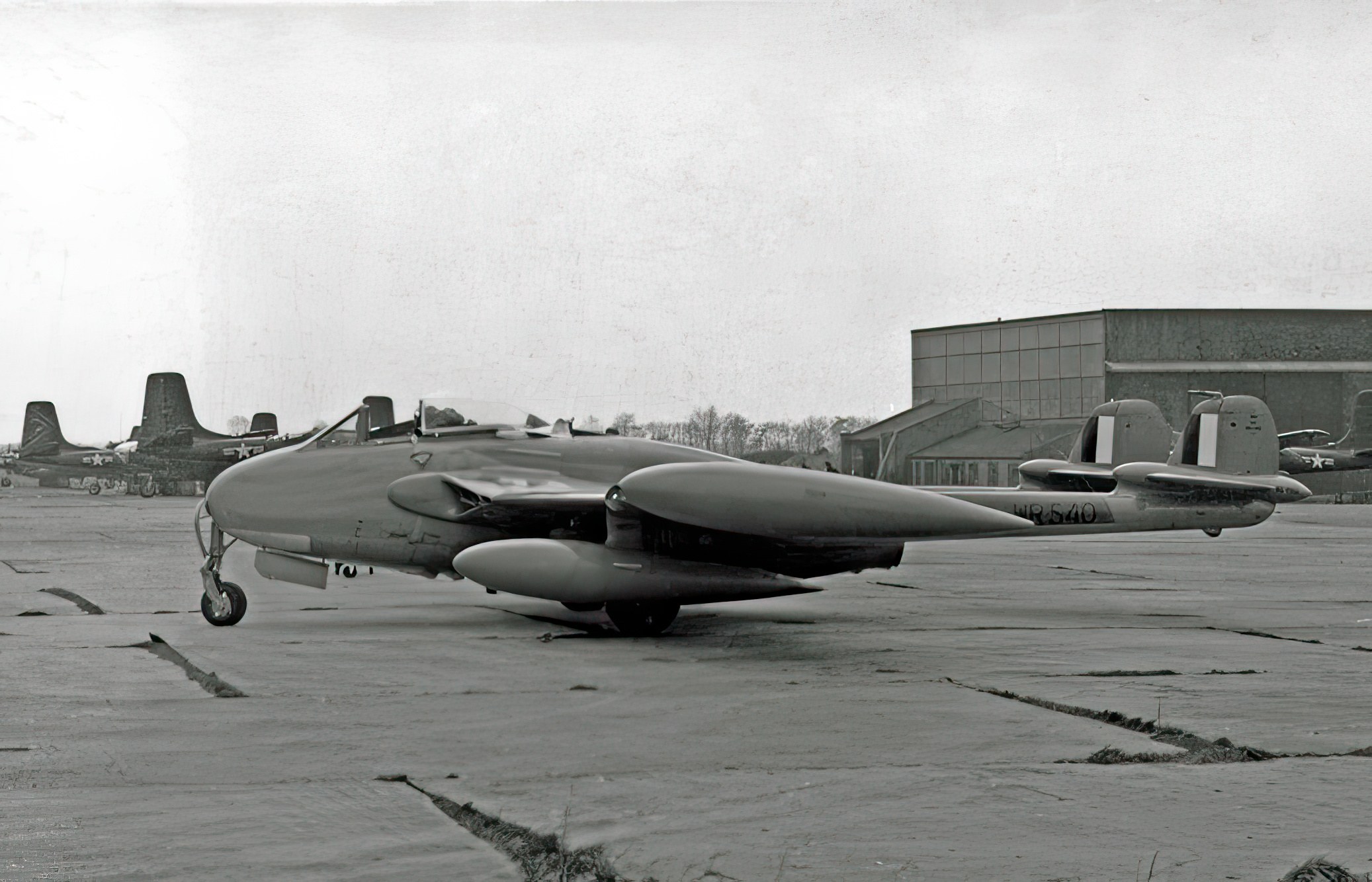 Black-and-white side view of de Havilland Venom WR540 parked near hangars.