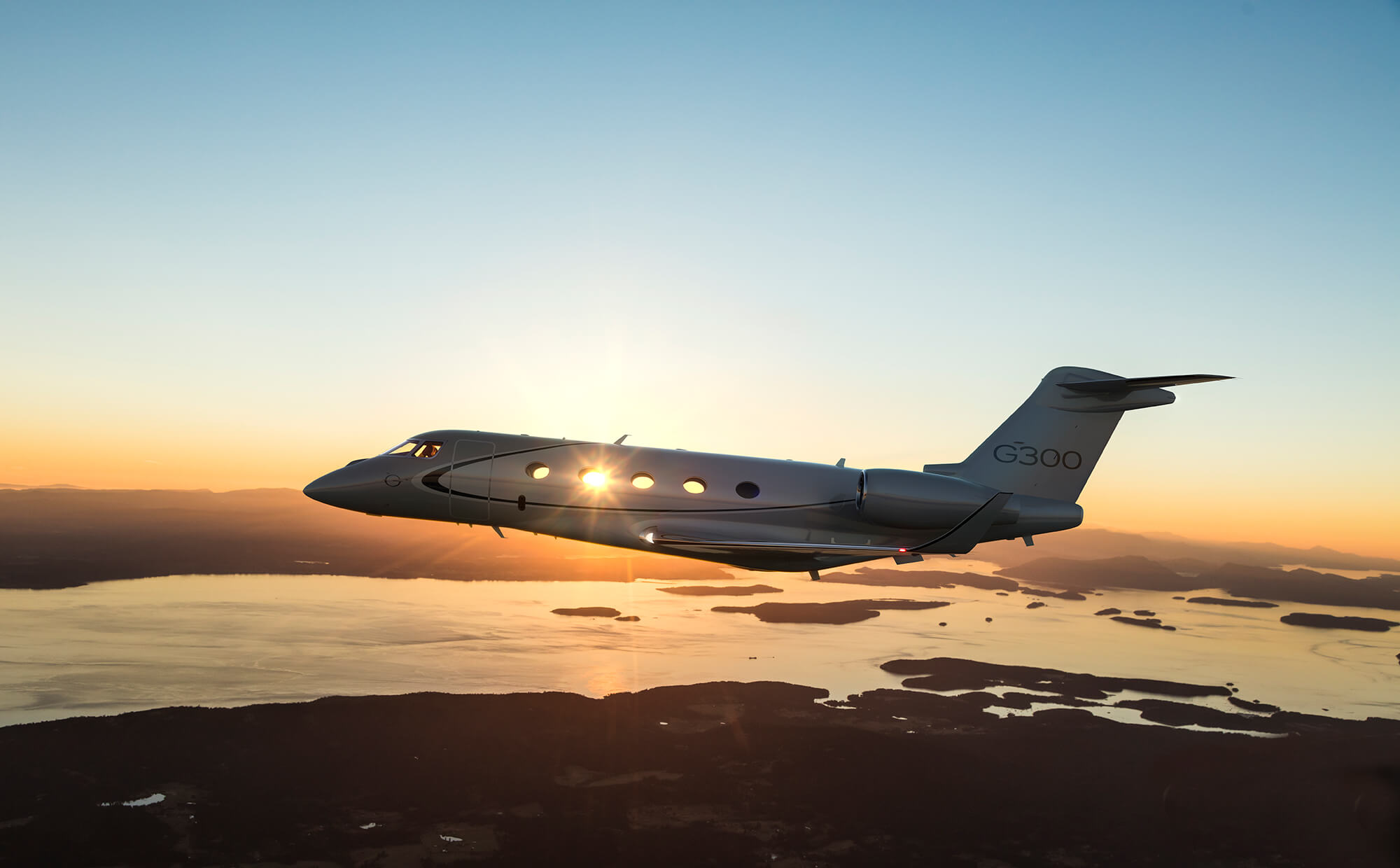 White Gulfstream business jet flying over water at sunset