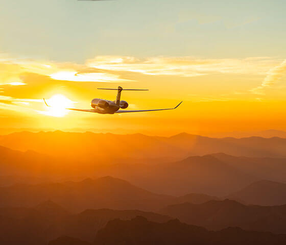 Gulfstream business jet flying toward the sun over mountains