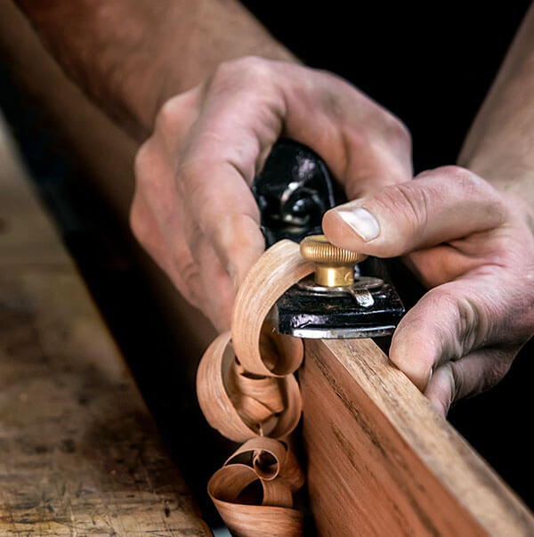 Hands shaping polished wood trim with a hand plane