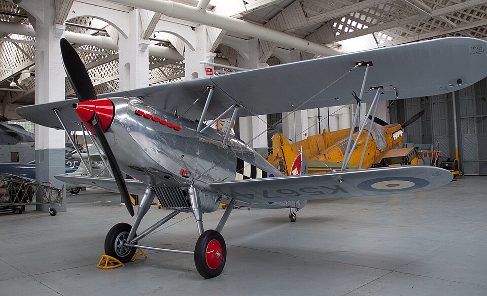 Hawker Fury biplane displayed indoors, showing one of Hawker's interwar fighter aircraft with open cockpit and fixed landing gear.