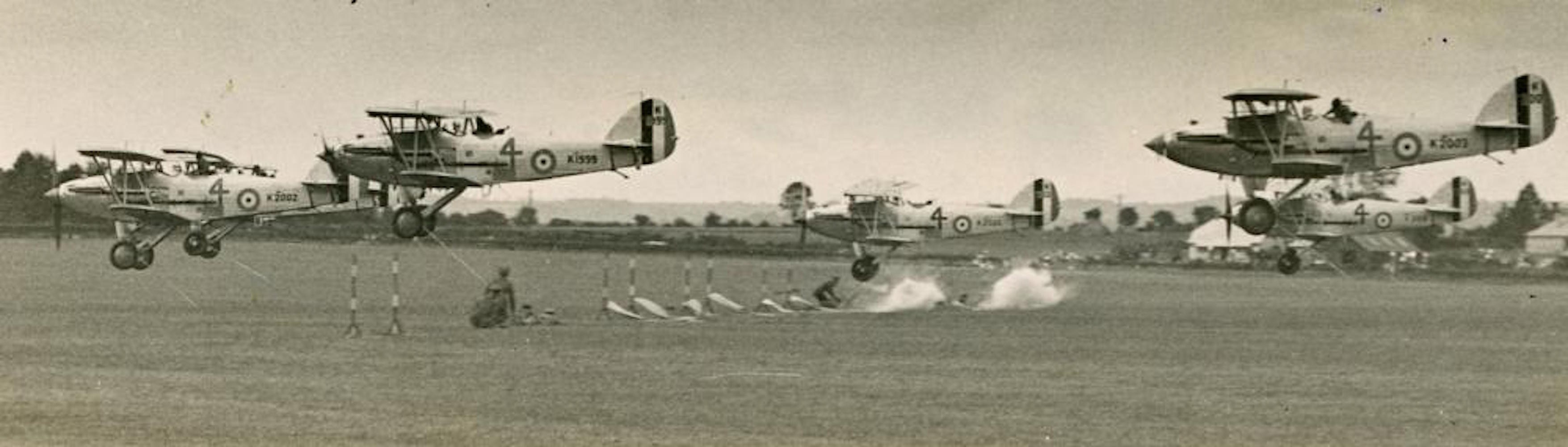 Black-and-white image of several Hawker Audax biplanes just above an airfield.
