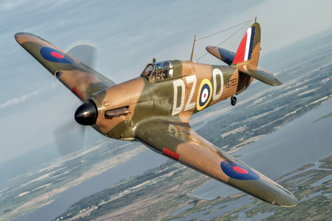 Camouflaged Hawker Hurricane marked DZ-D flying over water and coastline.