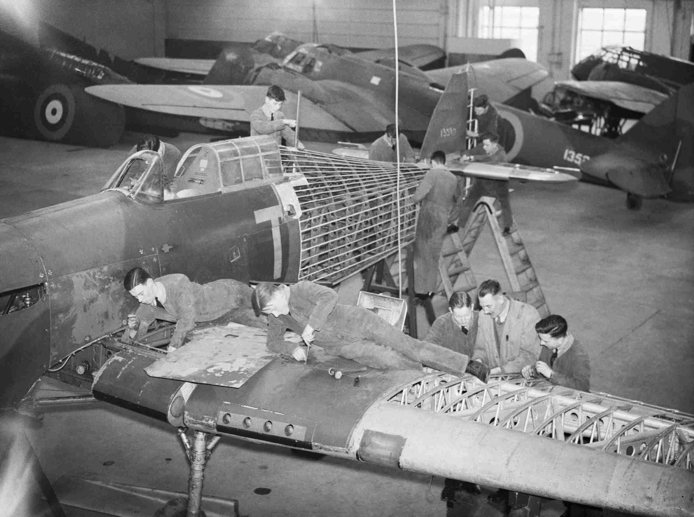 Black-and-white hangar scene with workers around Hawker Hurricane airframes.